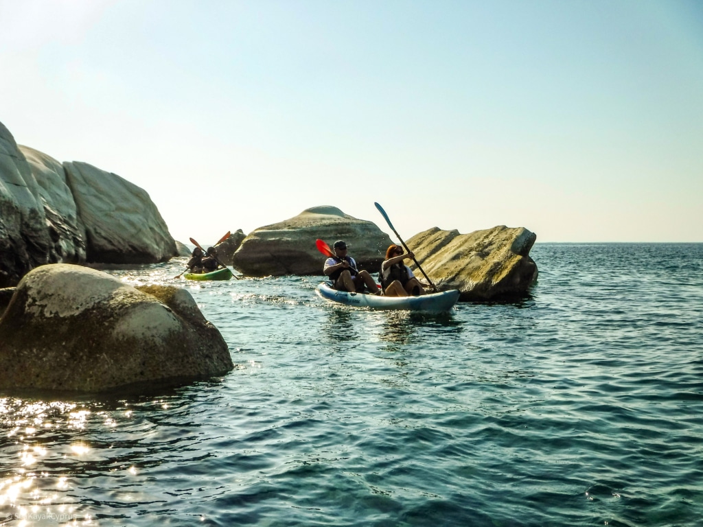 the ocean, with two canoes out at sea surrounded by rocks
