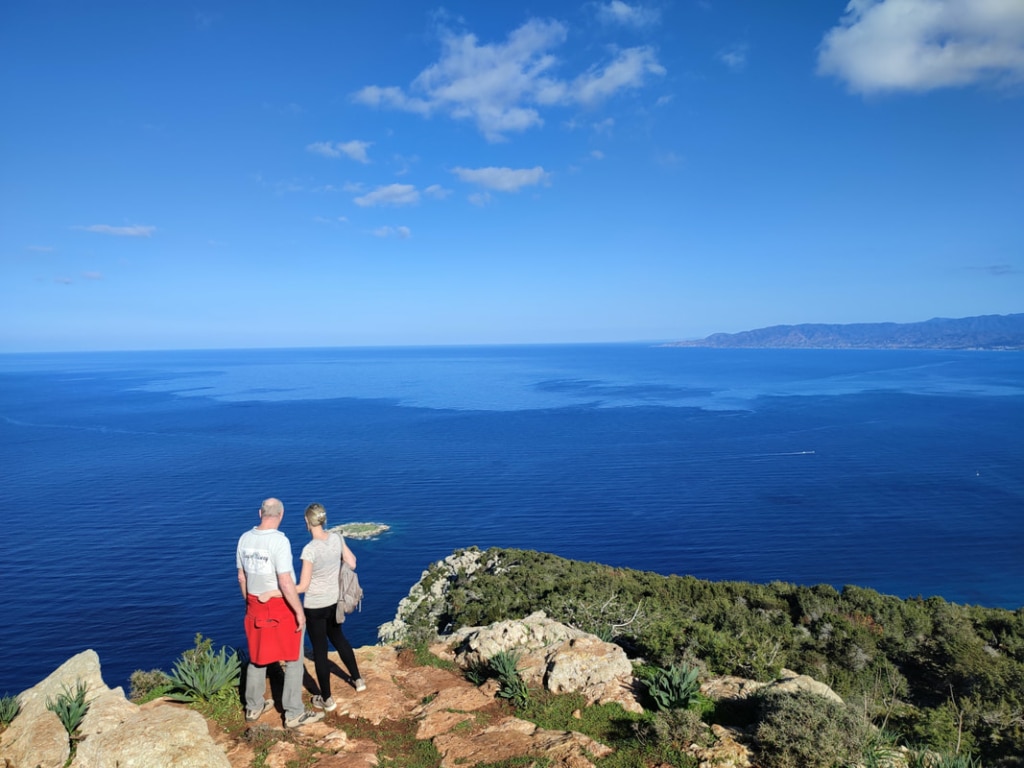 A couple standing on top of a cliff, looking out onto the sea