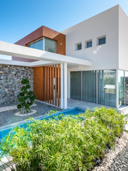 A villa, with a glass door along the side and some plants in the front.